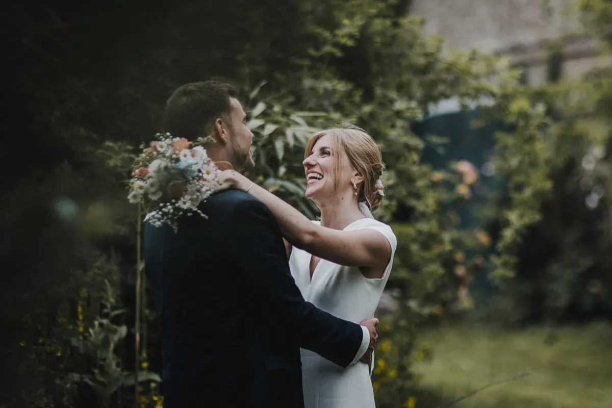 Hochzeitsreportage -- lachendes Brautpaar im Garten mit Blumenstrauß
